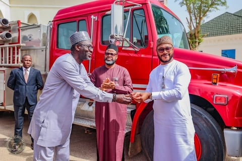 Four men in traditional attire shaking hands in front of a red truck during a formal presentation ceremony