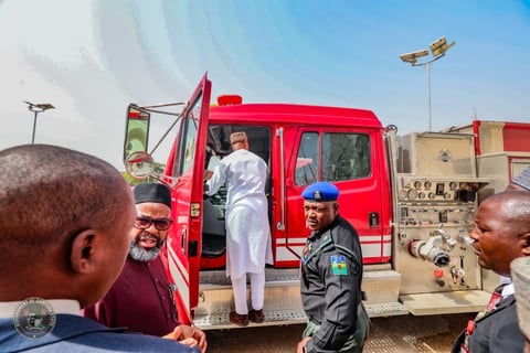 Official in white uniform boarding red emergency vehicle while military personnel and civilians observe at outdoor facility